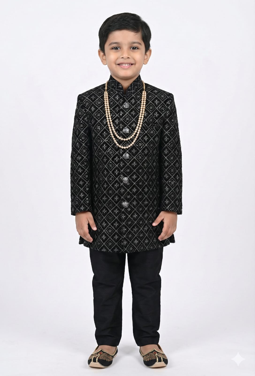 Young boy wearing a black embroidered sherwani with a white background