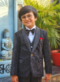 Child in formal attire standing outdoors with a Buddha statue and plants in the background