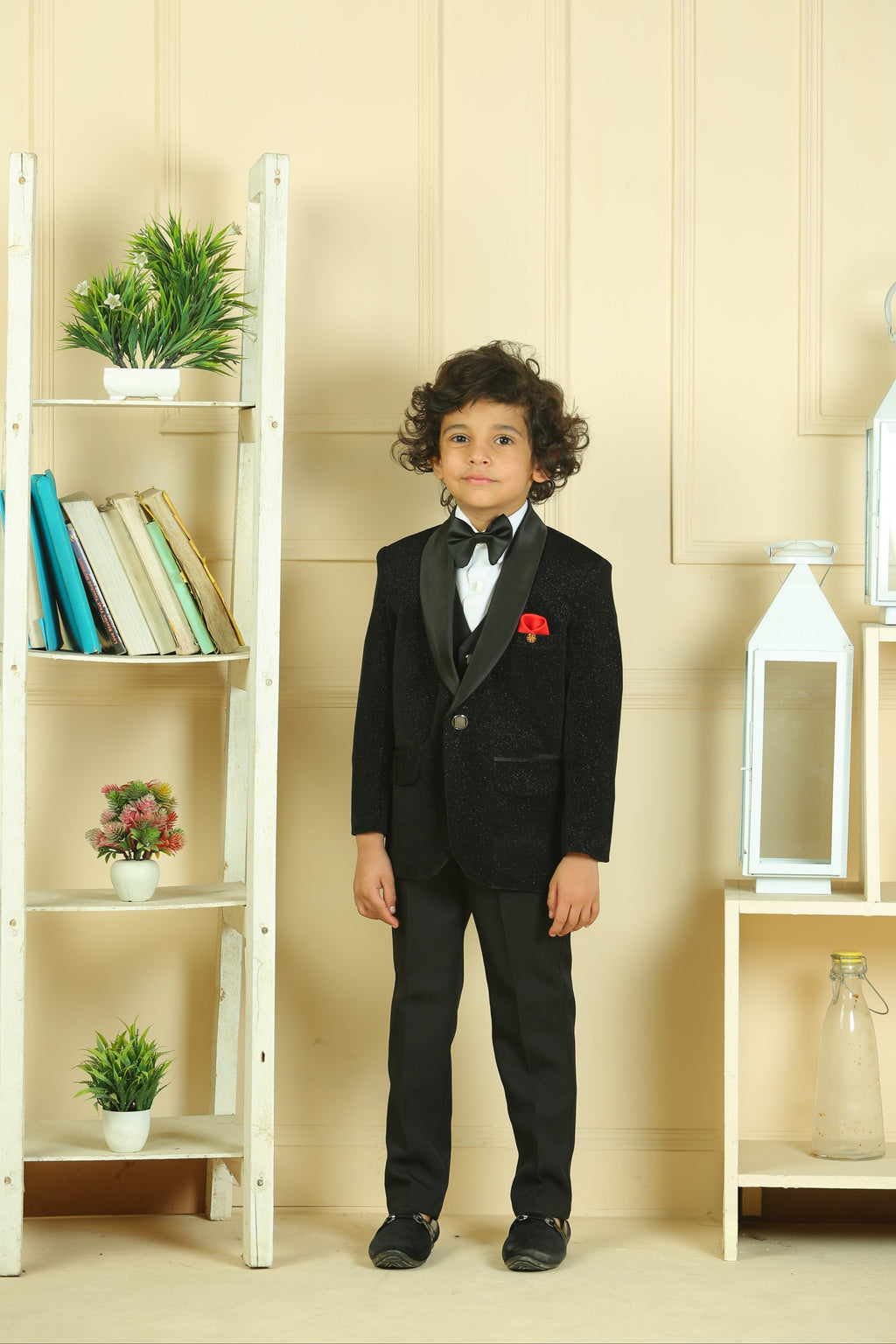 Child in a formal black suit standing in a room with shelves and decor.