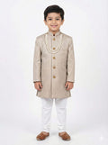 Young boy wearing a beige traditional sherwani with white pants on a light gray background