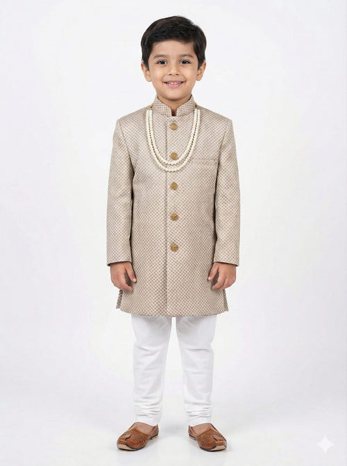 Young boy wearing a beige traditional sherwani with white pants on a light gray background
