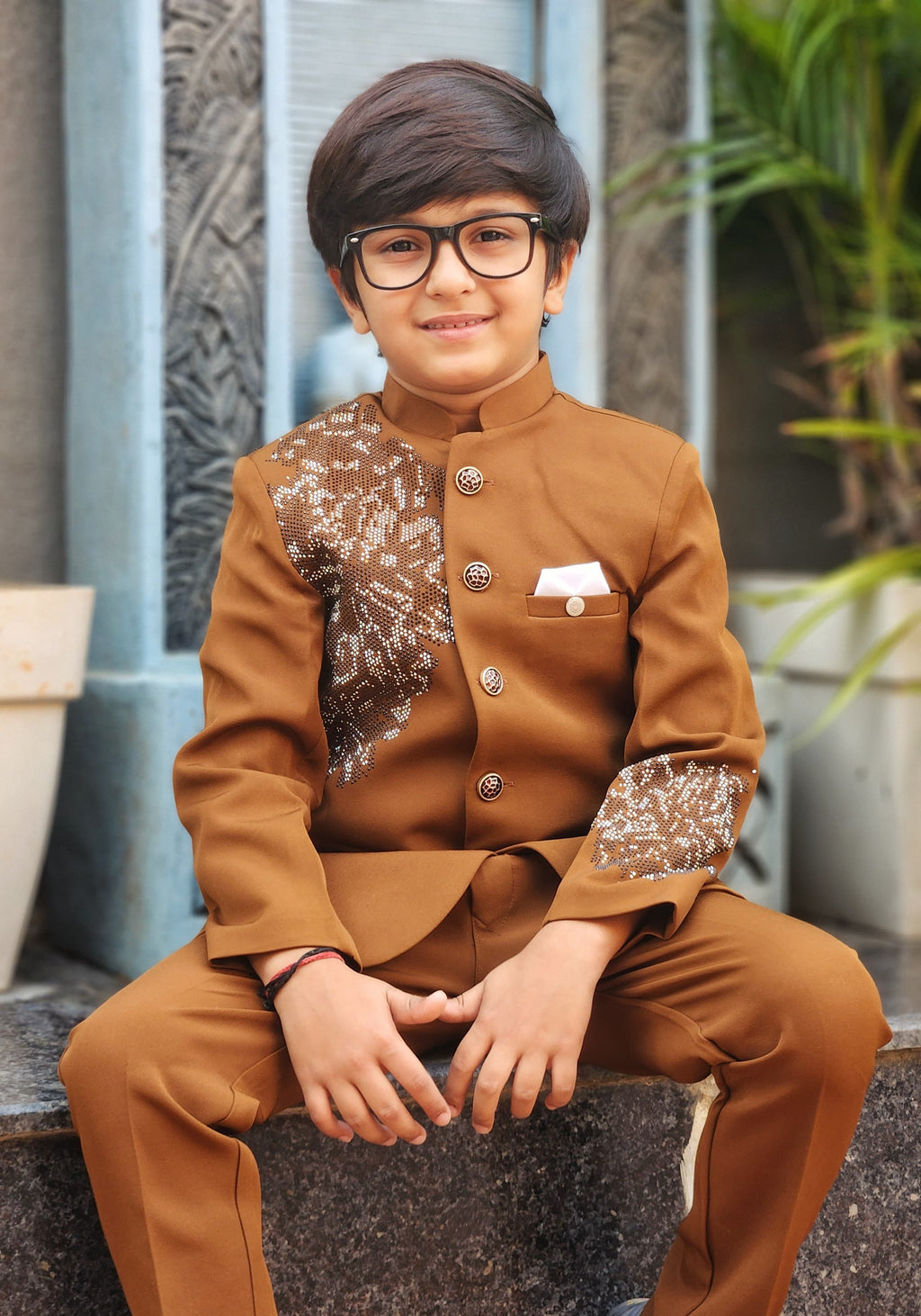 Child wearing a brown formal outfit with sequin details, sitting outdoors.