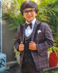 Child in a formal outfit with a plaid jacket and bow tie standing outdoors.