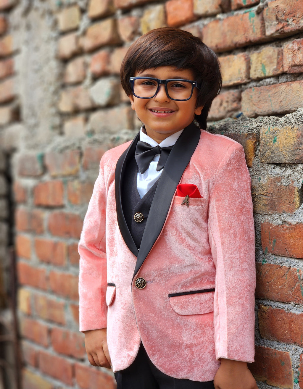 Child in a pink blazer and black vest standing against a brick wall