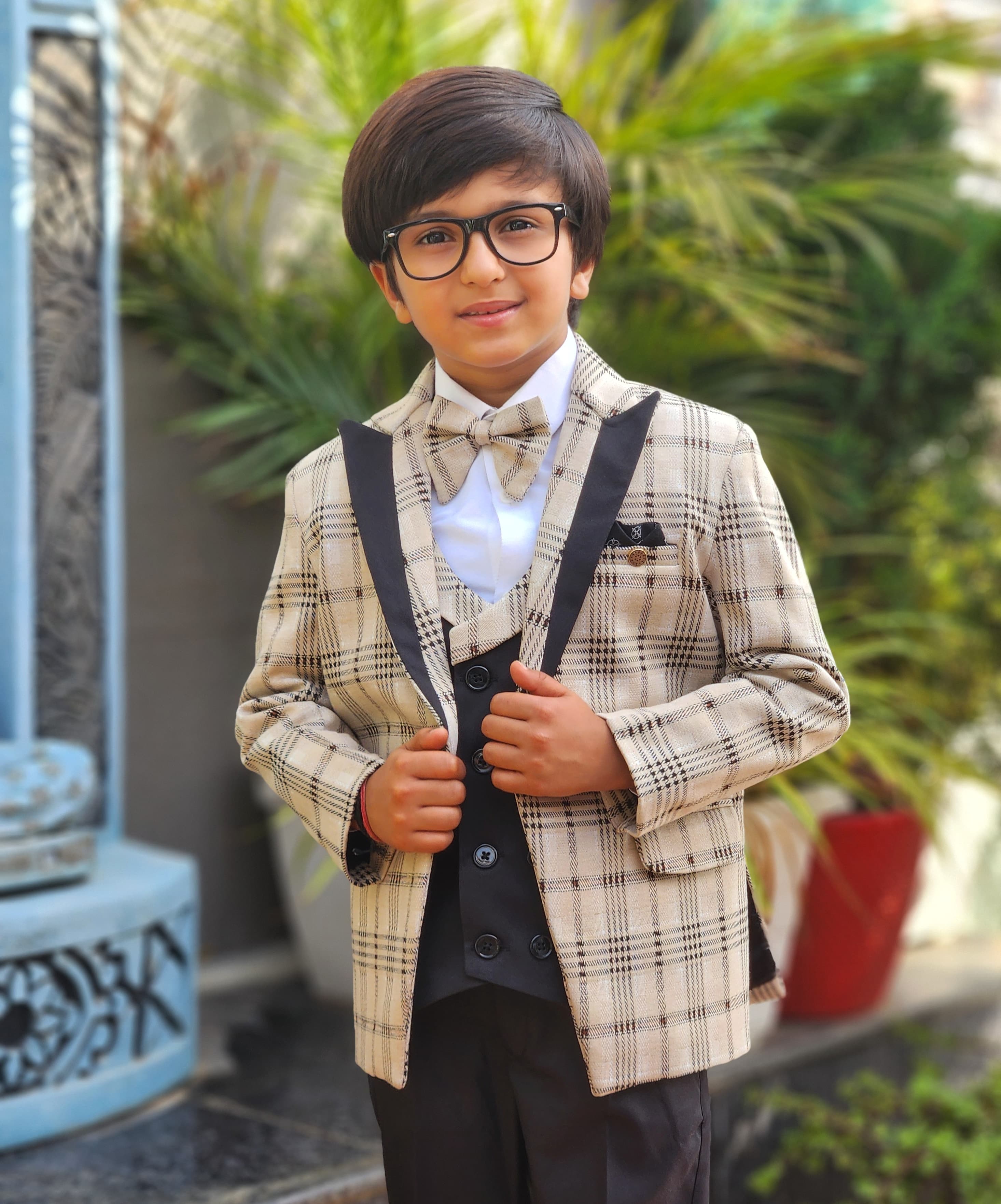 Child wearing a formal outfit with suspenders and bow tie in an outdoor setting.