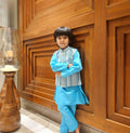Child in a blue traditional outfit standing against a wooden wall.