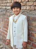 Child in a white traditional outfit standing against a brick wall