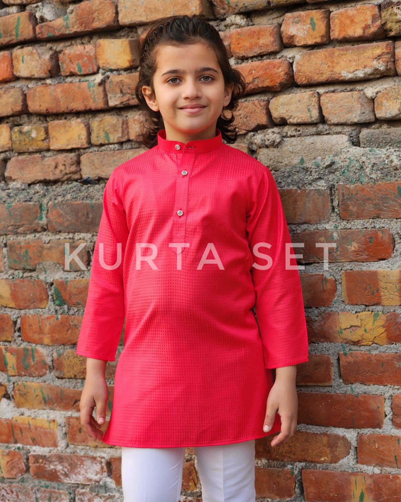 Child wearing a red kurta set standing against a brick wall with 'Kurta Set' text overlay.