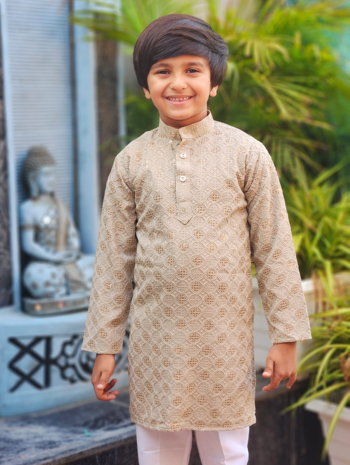 Young boy wearing a beige kurta with white pants standing outdoors.