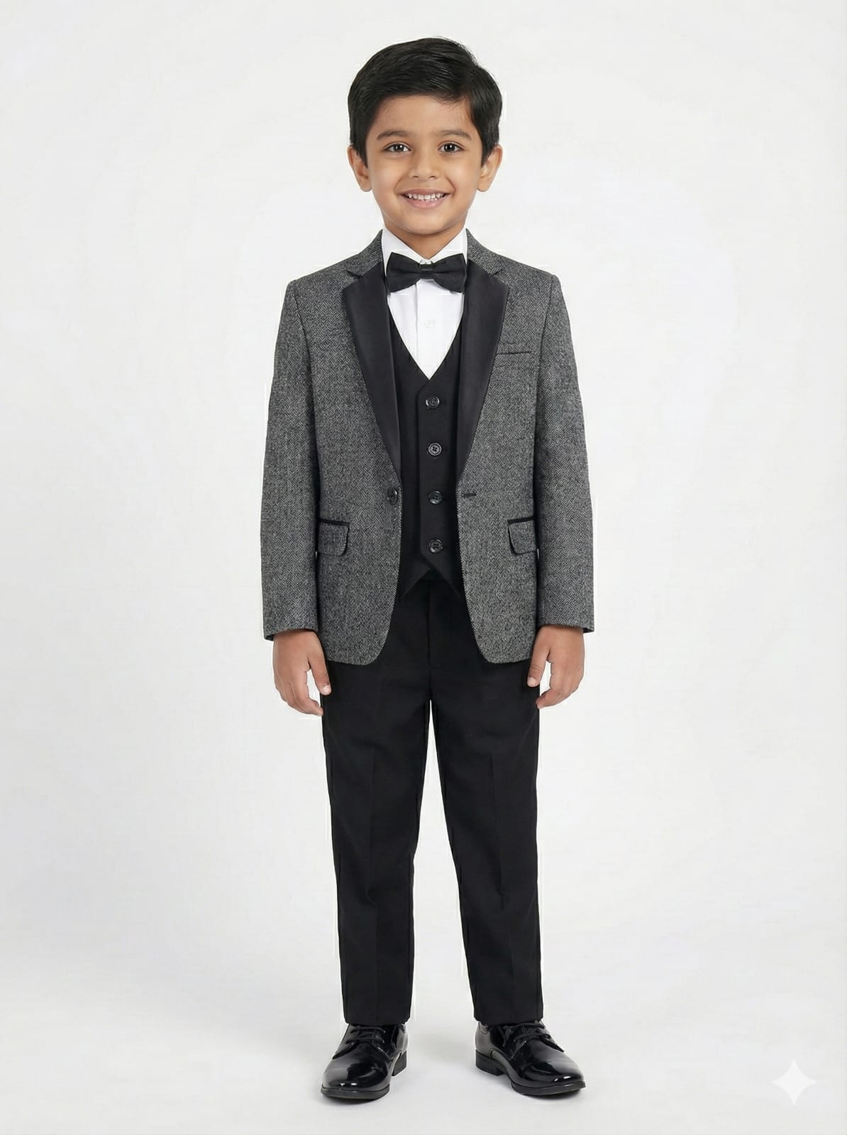 Young boy wearing a gray blazer, black vest, and pants on a white background