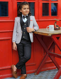 Child in formal attire leaning against a red wall with a table and mug.