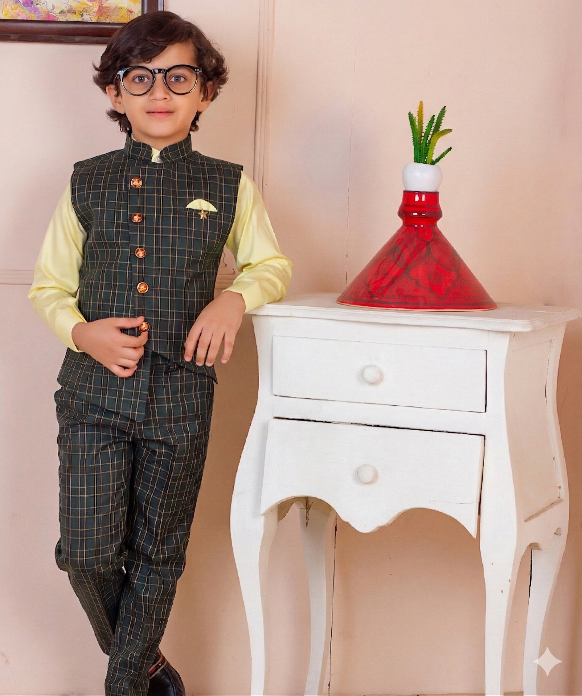 Child wearing a formal outfit standing next to a white cabinet with a red decorative item.