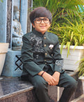 Child wearing a formal outfit sitting outdoors with plants in the background