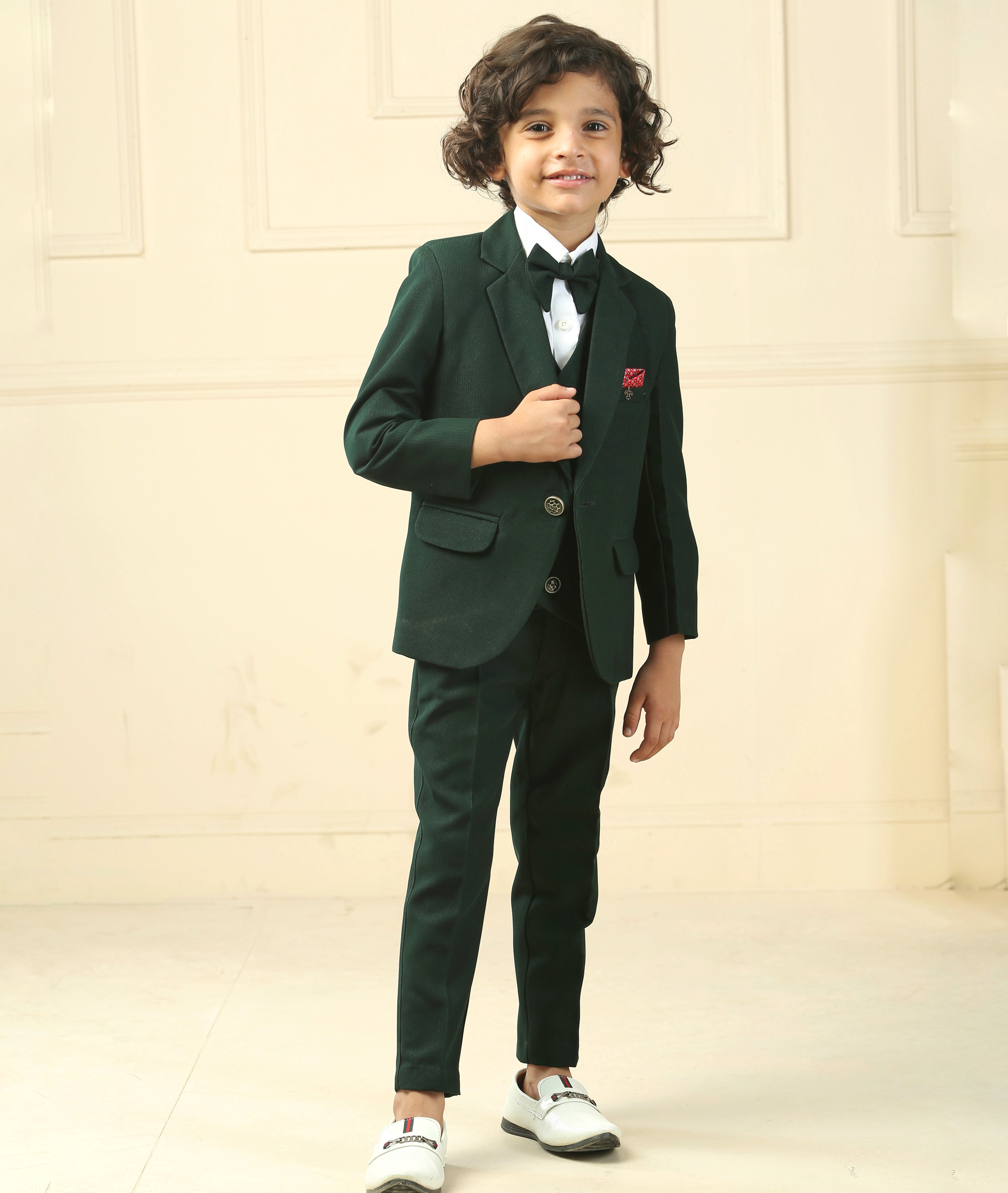 Child wearing a green suit with a white shirt and bow tie against a beige background