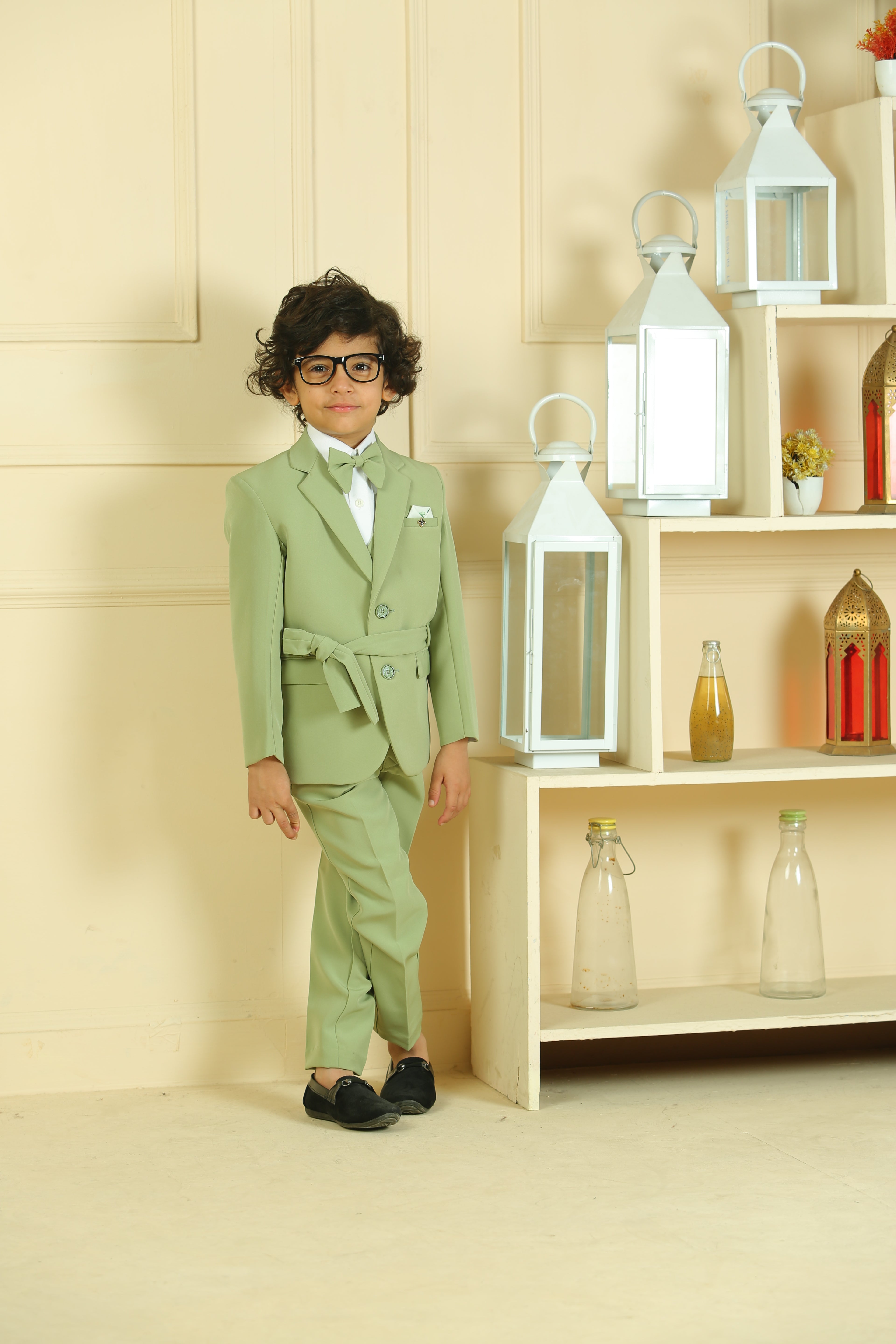 Child in a green suit standing in a room with shelves and lanterns.