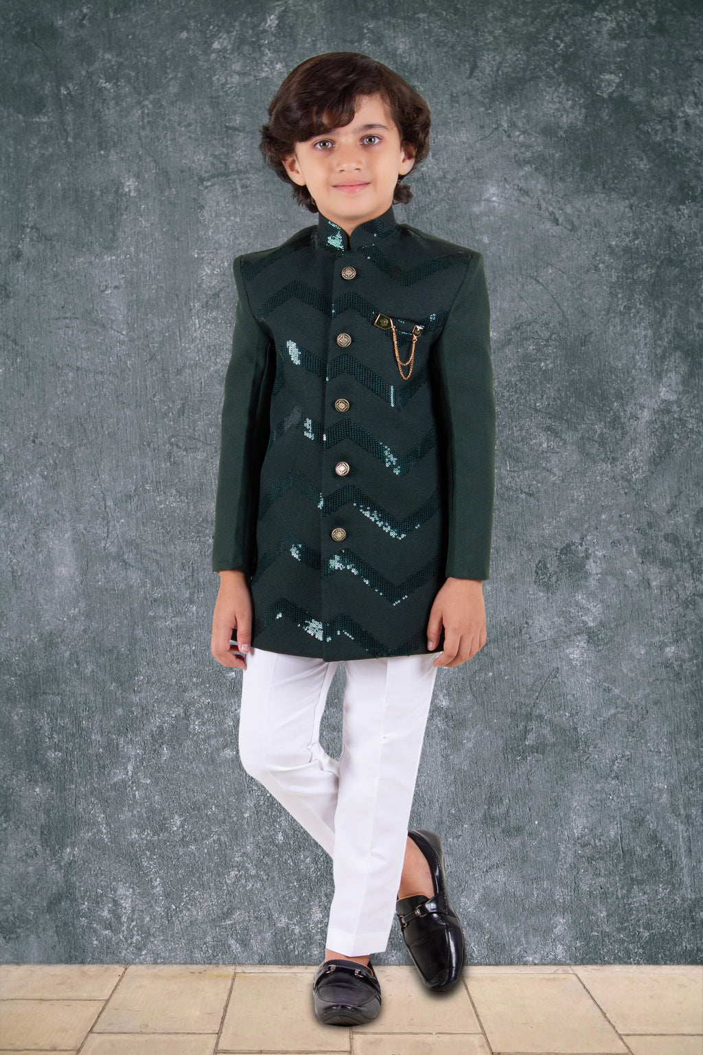 Child wearing a green traditional outfit with white pants against a gray background
