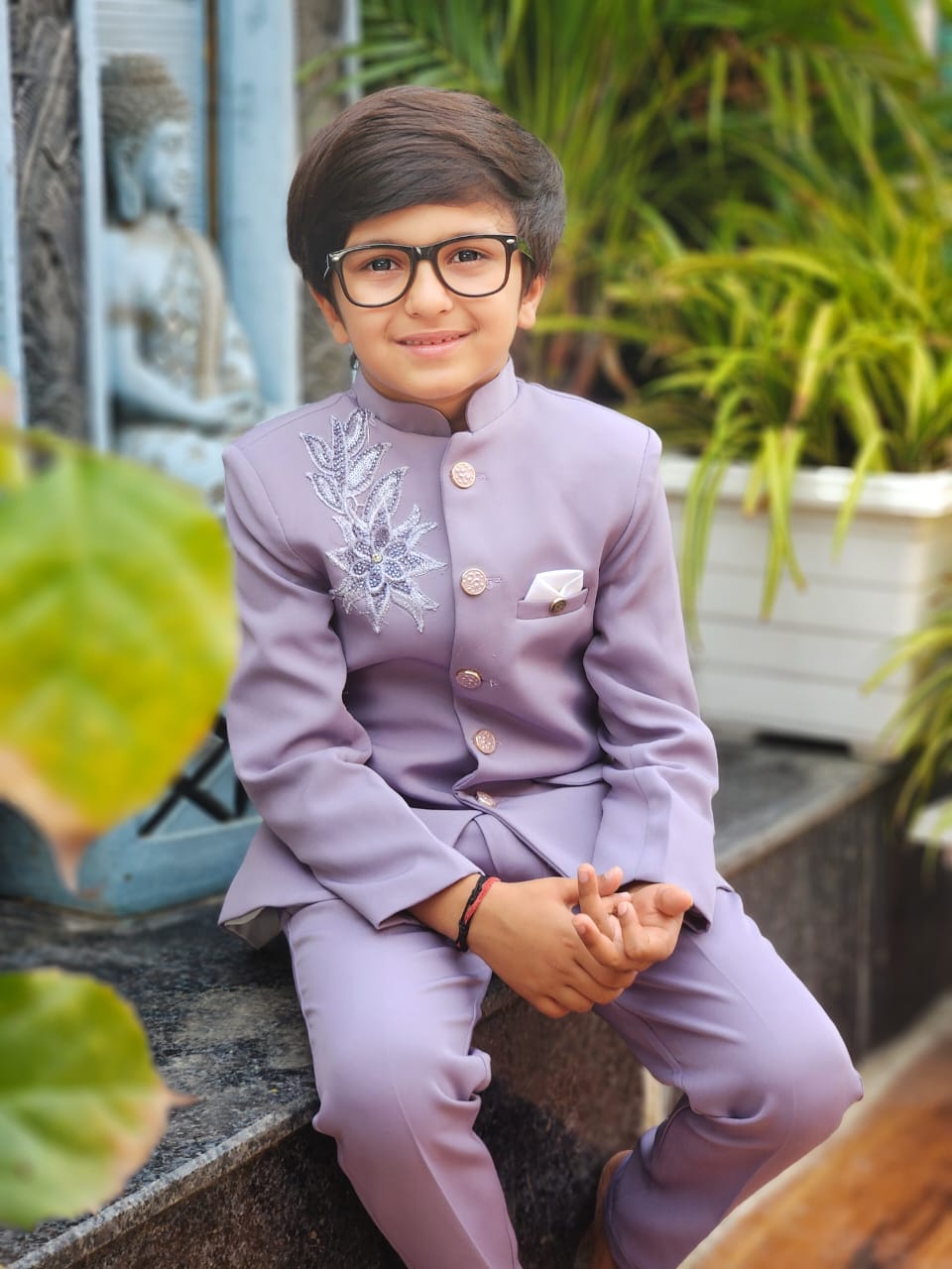 Child wearing a light purple formal outfit with a floral design, sitting outdoors.