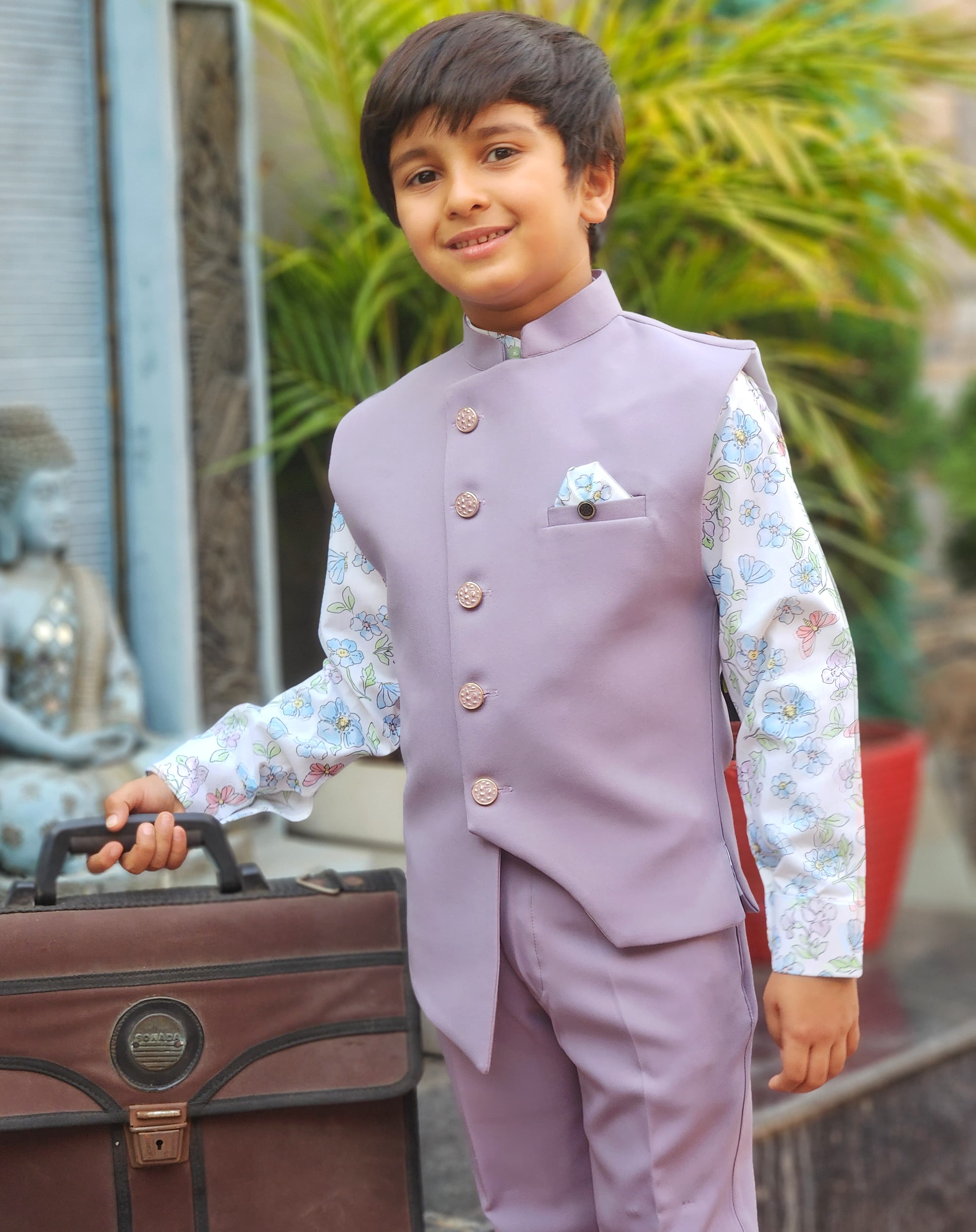 Young boy in a formal outfit standing next to a suitcase with a blurred background