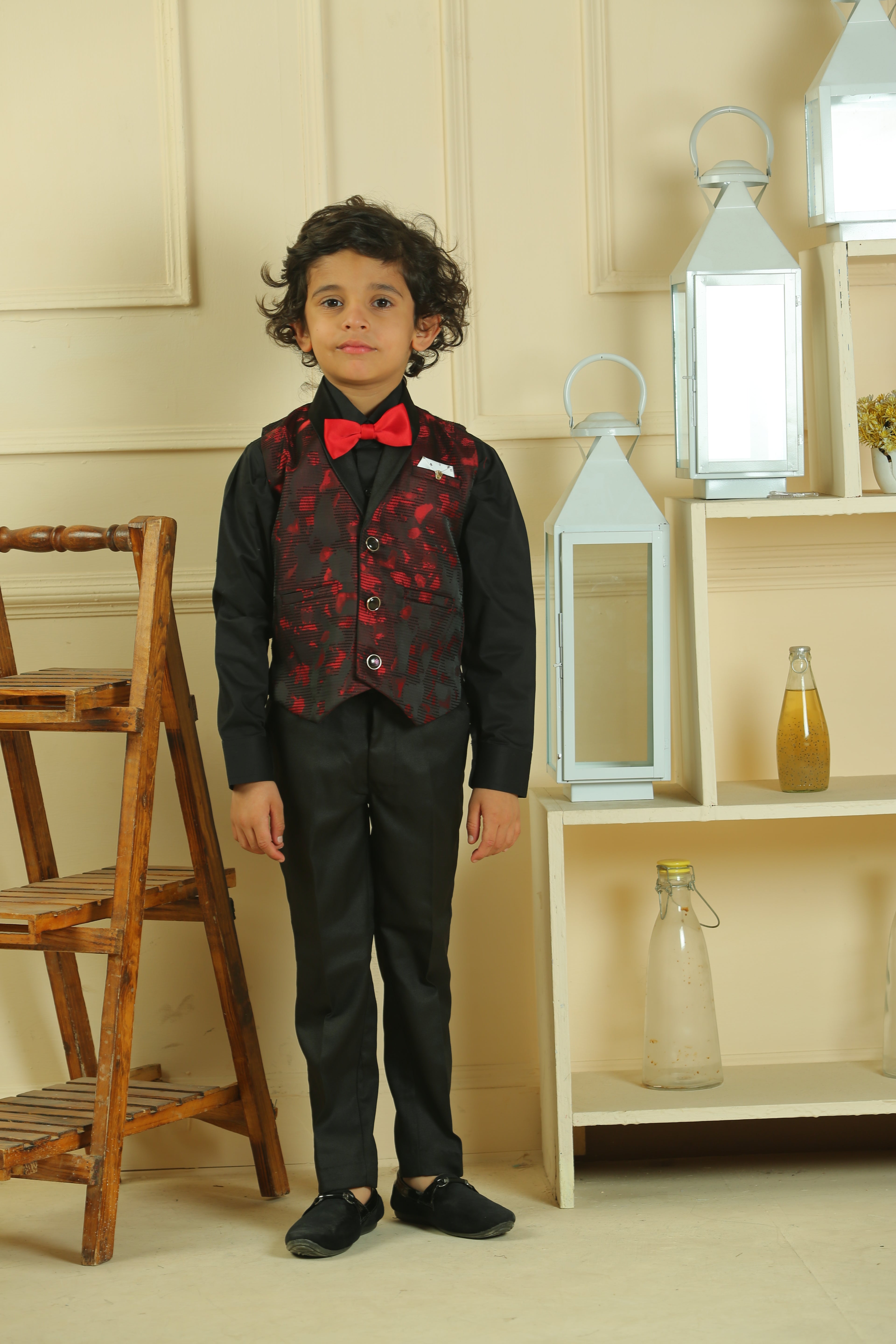 Person wearing a black suit with a red bow tie in a room with wooden chairs and shelves.