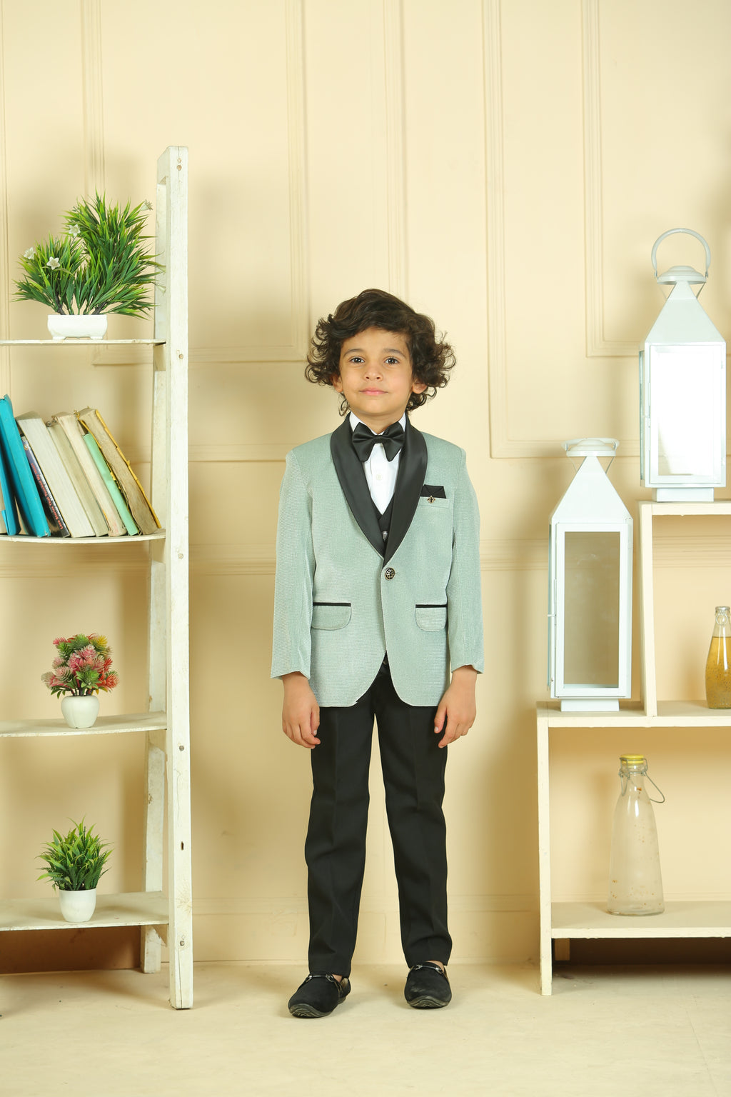 Young boy in a light green suit standing in a room with shelves and plants.