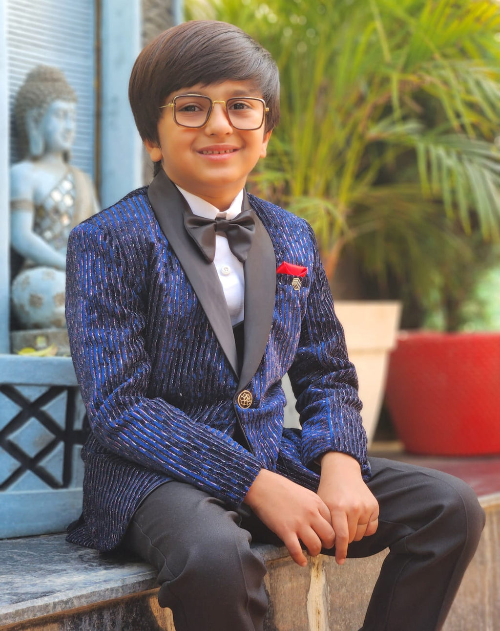 Young boy in a blue suit with a bow tie sitting outdoors.
