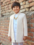 Young boy in traditional attire standing against a brick wall