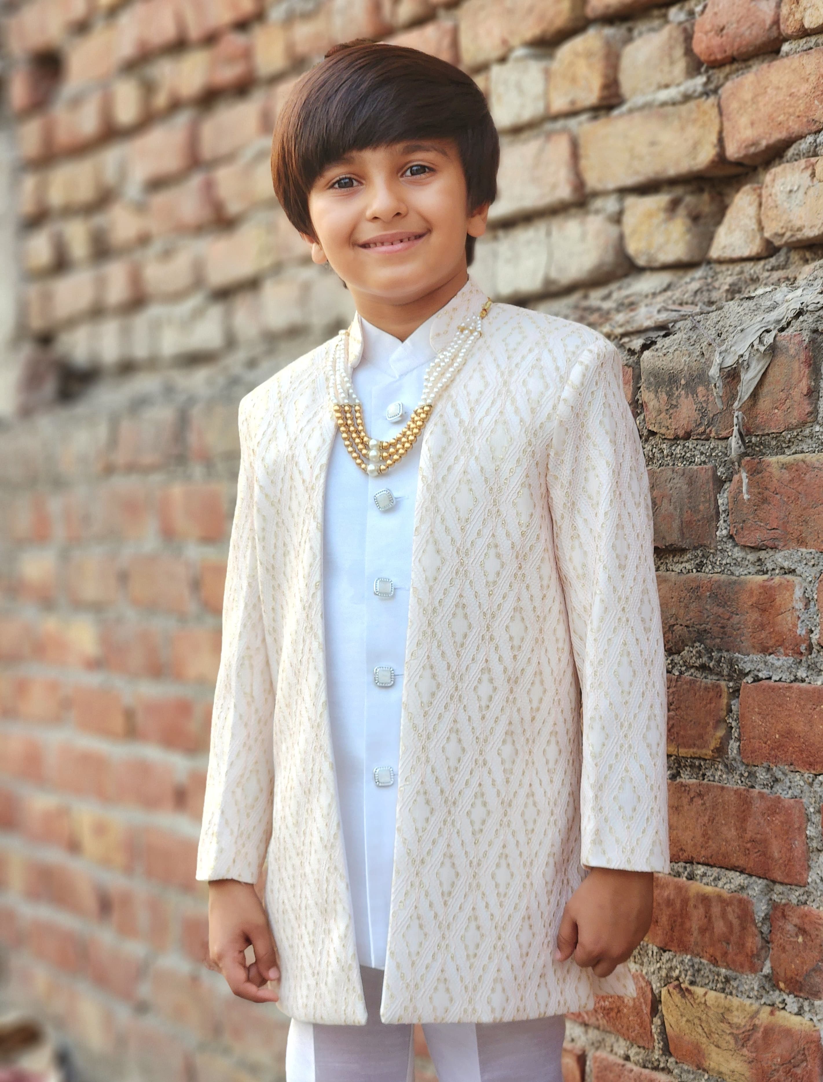 Young boy in traditional attire standing against a brick wall
