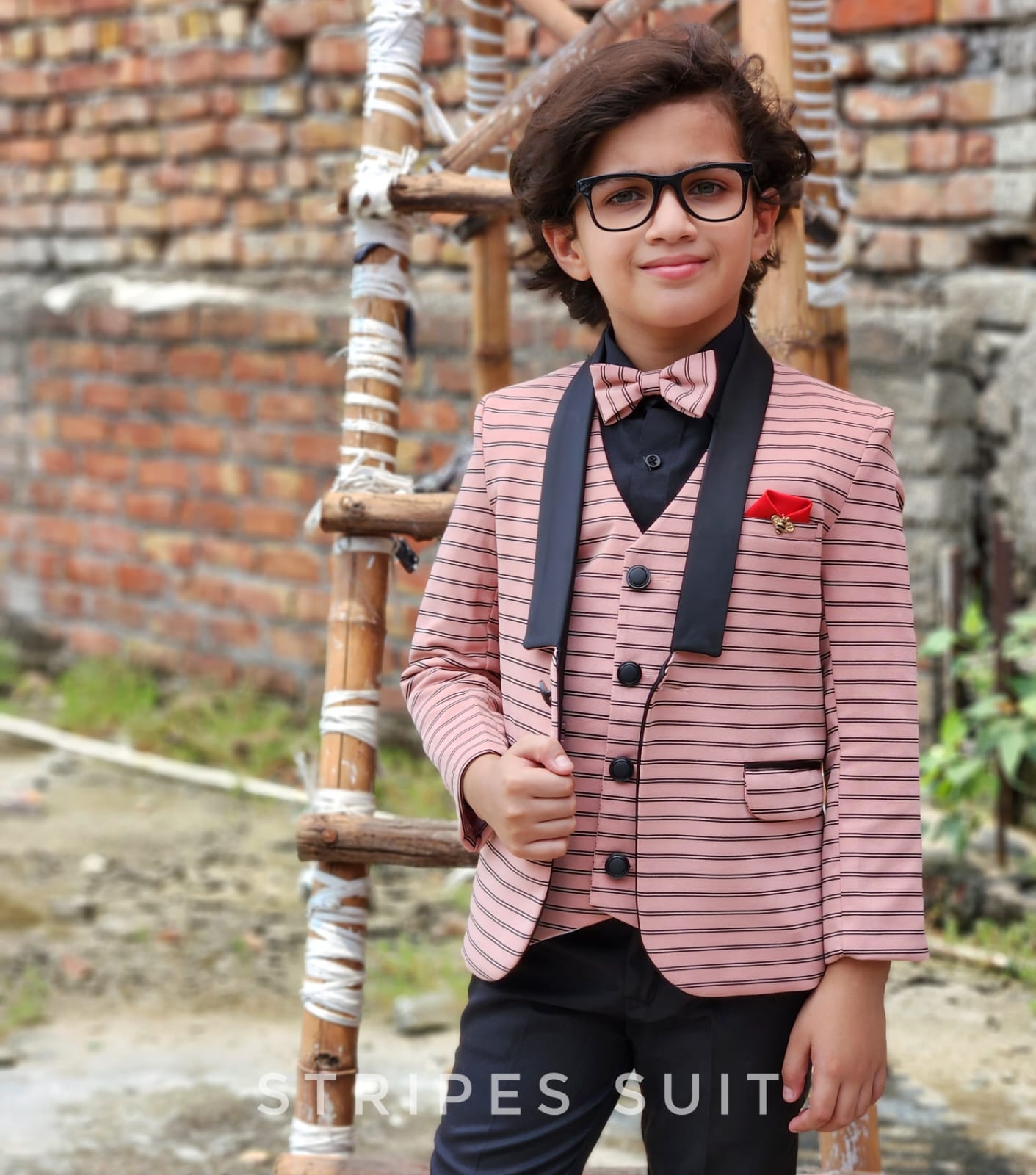 Child wearing a striped suit with a bow tie in front of a brick wall.