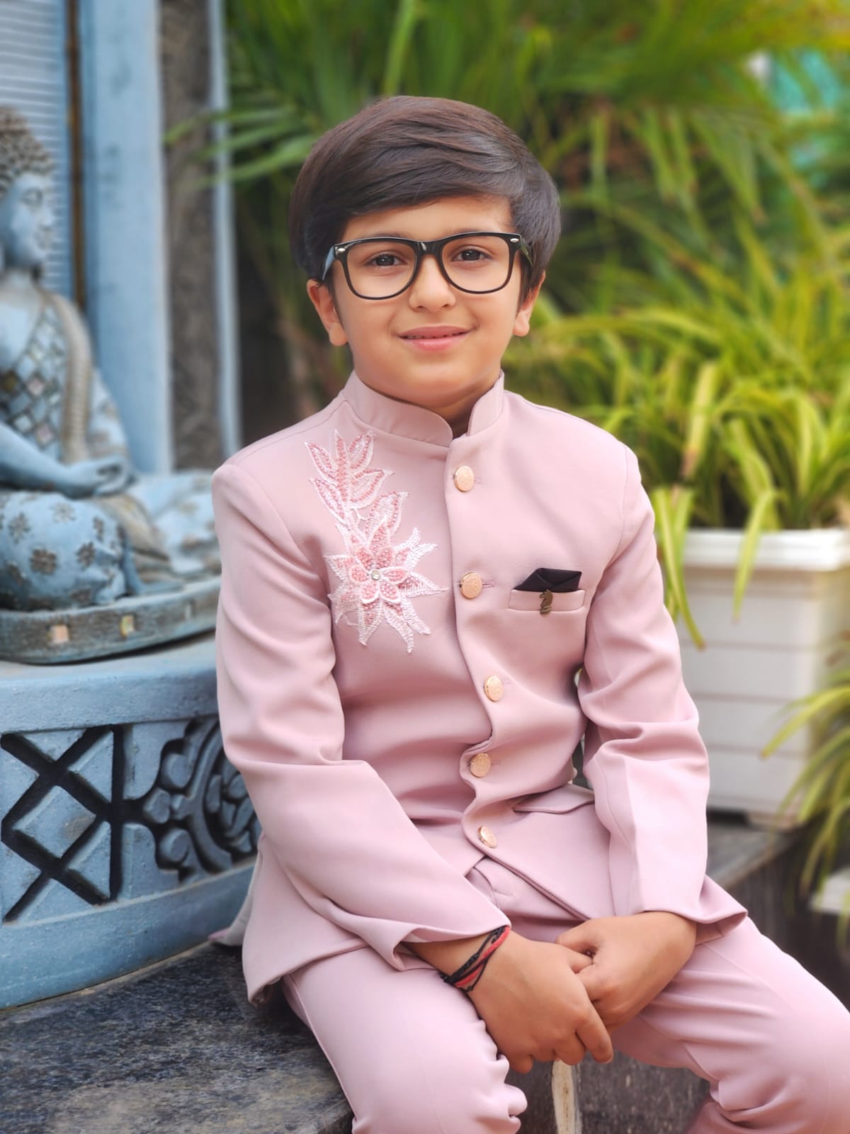 Child wearing a pink traditional outfit with a decorative flower design, sitting outdoors.