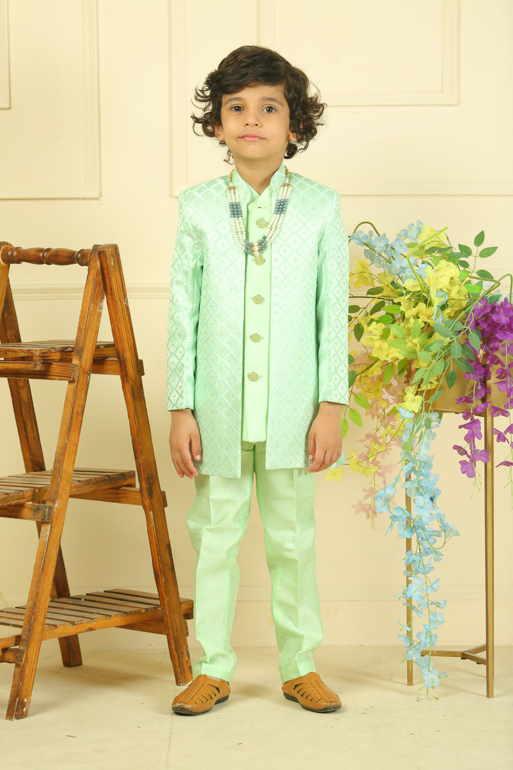 Person wearing a light green outfit with floral patterns, standing next to a wooden chair and floral decorations.