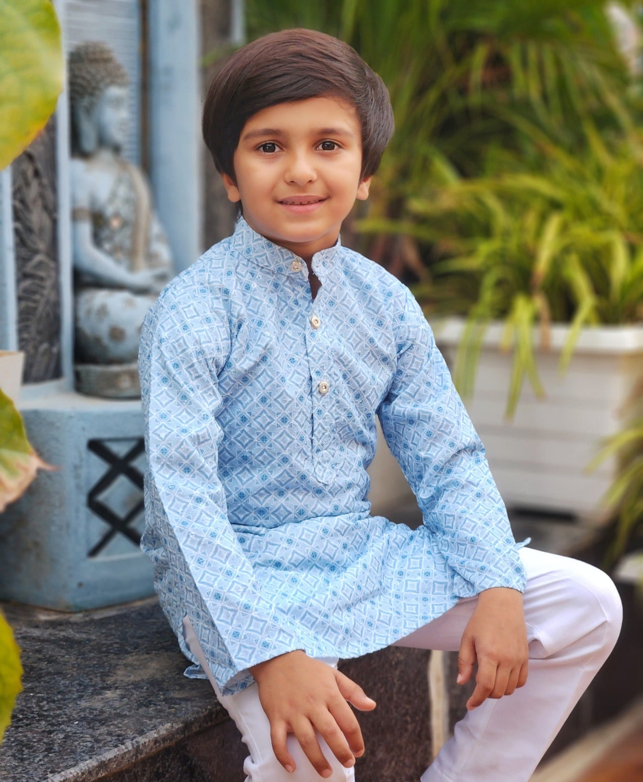Child wearing a light blue kurta with white pants sitting outdoors.