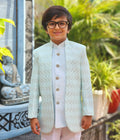 Child wearing a light blue patterned blazer and white shirt outdoors with plants and a statue in the background.