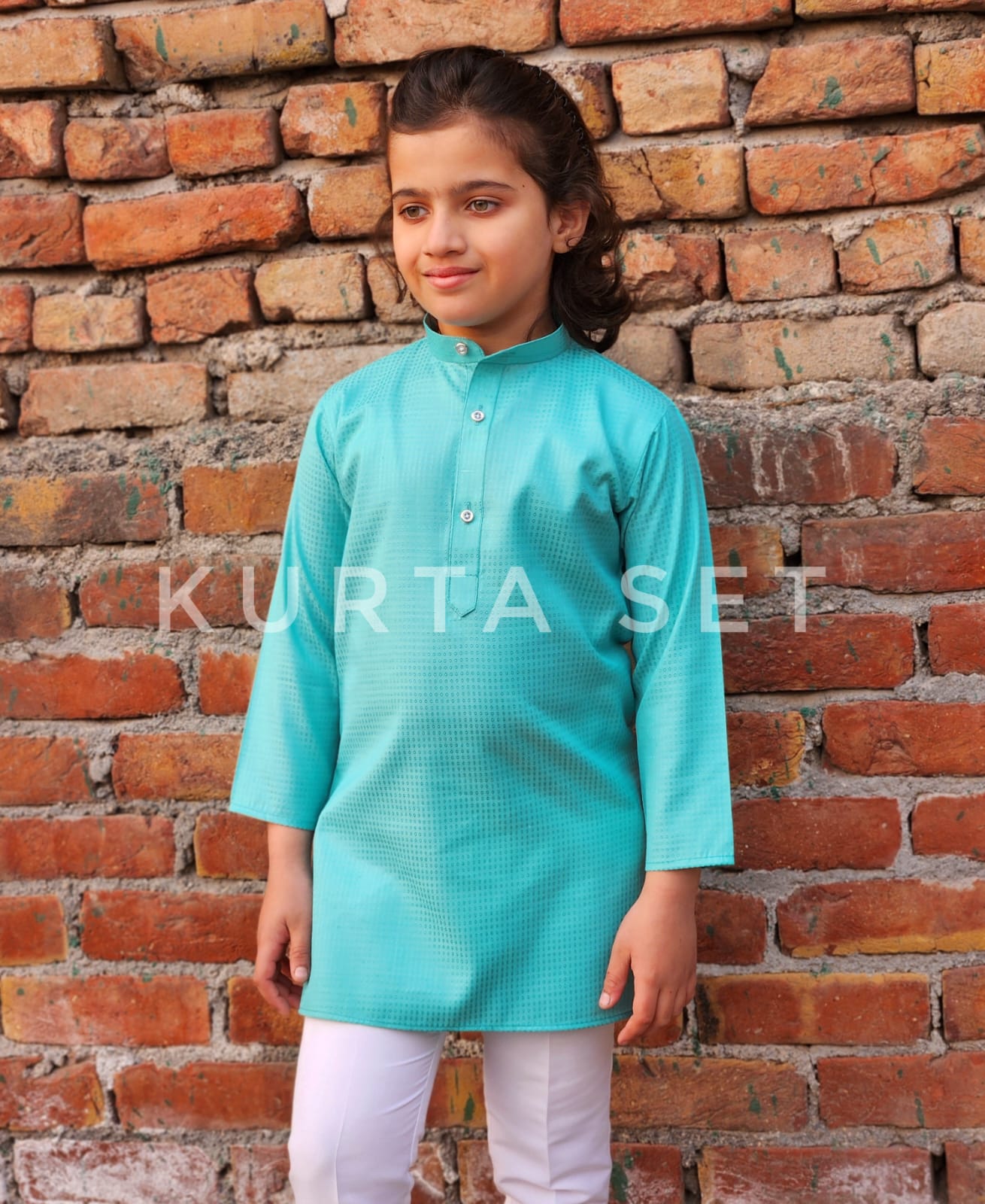 Child wearing a turquoise kurta against a brick wall with 'Kurta Set' text overlay.