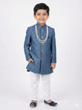 Young boy wearing a blue traditional outfit with white pants on a white background
