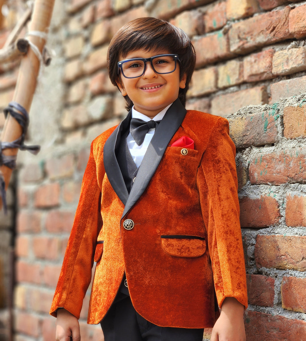 Child wearing an orange blazer and black bow tie against a brick wall.