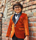 Child wearing an orange blazer and black bow tie against a brick wall.